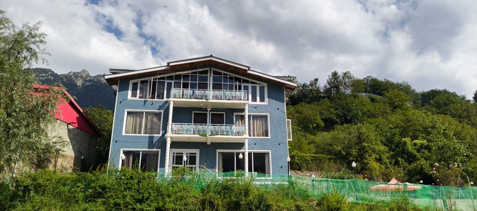 Hotel Rafting Heights Pahalgam exterior set against green hills and Himalayan mountain backdrop